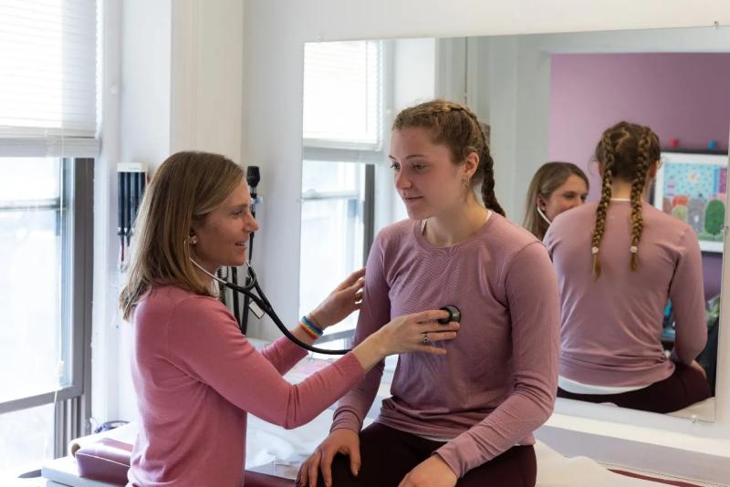 a doctor listening to a teen girls heart with a stethoscope